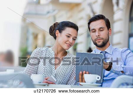 Stock Photograph - Businessman discussing plans over digital tablet to businesswoman while sitting and waiting for their food at restaurant. Fotosearch