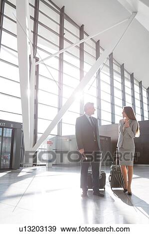 Stock Photo - Businessman discussing plans with businesswoman in airport . Fotosearch