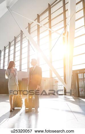 Stock Photo - Businessman discussing plans with businesswoman in airport . Fotosearch