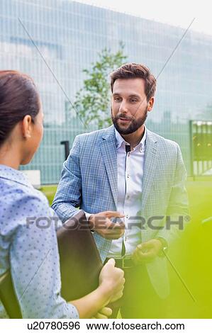 Stock Photograph - Businessman discussing plans with businesswoman on meeting outdoor. Fotosearch