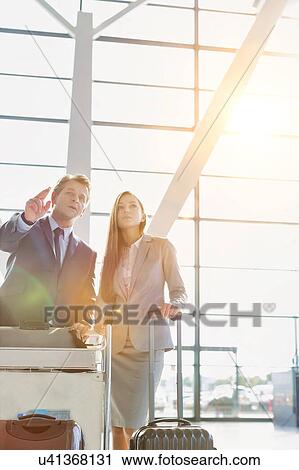 Stock Image - Businessman gesturing and talking to young attractive businesswoman while queuing for check in at airport. Fotosearch