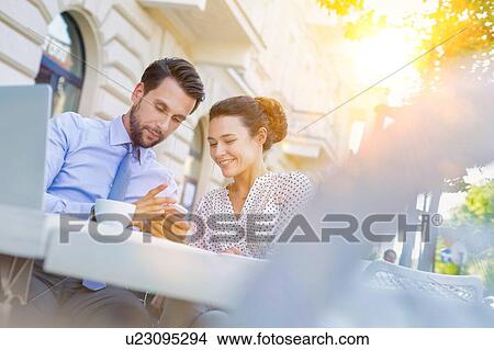 Picture - Businessman showing smartphone to businesswoman while having coffee during office break. Fotosearch