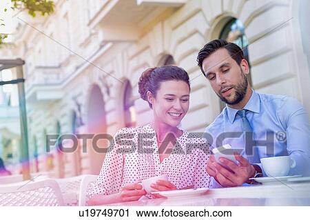 Stock Image - Businessman showing smartphone to businesswoman while having coffee during office break. Fotosearch