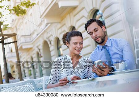 Stock Image - Businessman showing smartphone to businesswoman while having coffee during office break. Fotosearch