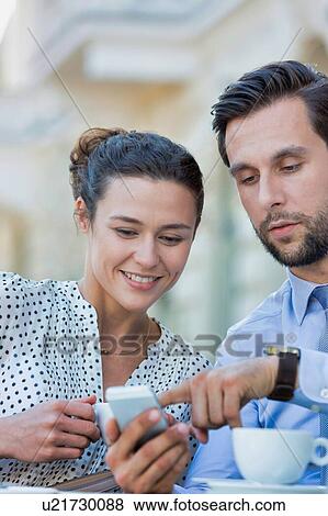 Businessman showing smartphone to businesswoman while having coffee during office break View Large Photo Image Stock Photo - Businessman showing smartphone to businesswoman while having coffee during office break. Fotosearch