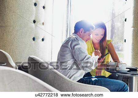 Stock Photo - Businessman showing smartphone to businesswoman while sitting in coffee shop. Fotosearch