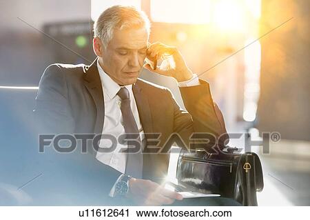 Businessman talking on smartphone while sitting and waiting in his gate for boarding in airport View Large Photo Image Stock Image - Businessman talking on smartphone while sitting and waiting in his gate for boarding in airport. Fotosearch