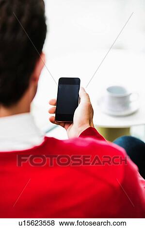 Stock Photo - Businessman using smartphone while sitting and drinking coffee in lobby. Fotosearch