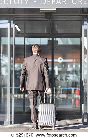 Businessman walking with his luggage in departure area at airport View Large Photo Image Stock Image - Businessman walking with his luggage in departure area at airport. Fotosearch