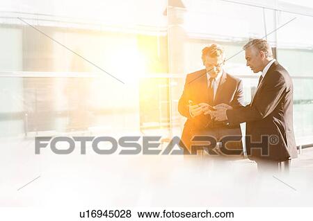 Stock Photo - Businessmen discussing plans over smartphone in the airport. Fotosearch