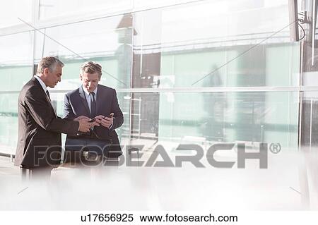 Businessmen discussing plans over smartphone in the airport View Large Photo Image Stock Photography - Businessmen discussing plans over smartphone in the airport. Fotosearch