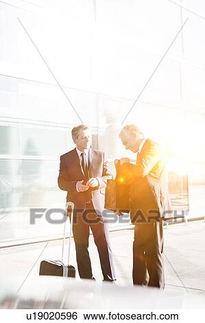 Businessmen standing while talking in the airport View Large Photo Image Stock Photograph - Businessmen standing while talking in the airport. Fotosearch