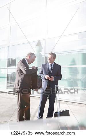 Stock Photography - Businessmen standing while talking in the airport. Fotosearch