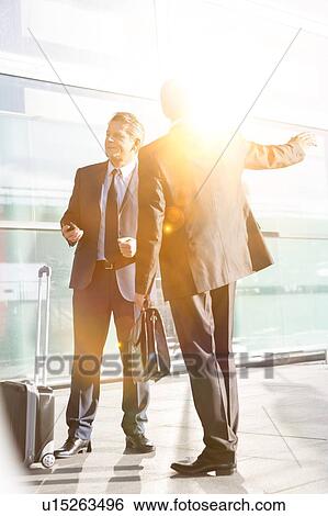 Stock Photograph - Businessmen talking while waiting for taxi in the airport. Fotosearch