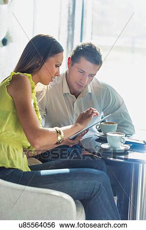 Businesswoman discussing plans over digital tablet to businessman while sitting and drinking coffee View Large Photo Image Stock Photograph - Businesswoman discussing plans over digital tablet to businessman while sitting and drinking coffee . Fotosearch
