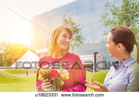 Stock Image - Businesswoman holding boquet of flowers while talking to her friend. Fotosearch