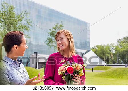 Businesswoman holding boquet of flowers while talking to her friend View Large Photo Image Stock Photo - Businesswoman holding boquet of flowers while talking to her friend. Fotosearch
