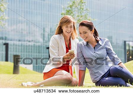 Businesswoman laughing while showing smartphone to her colleague View Large Photo Image Picture - Businesswoman laughing while showing smartphone to her colleague. Fotosearch