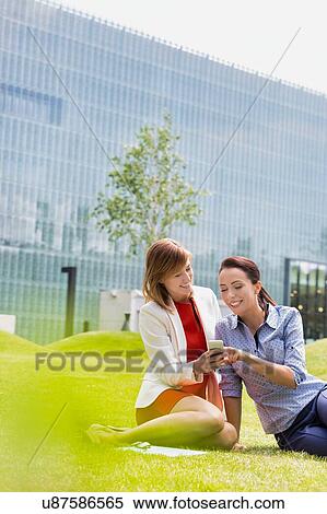 Stock Photography - Businesswoman laughing while showing smartphone to her colleague. Fotosearch