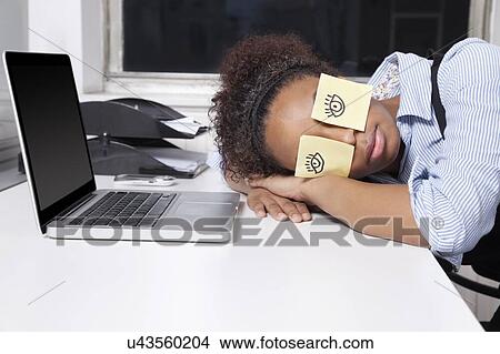 Picture - Businesswoman sleeping with sticky notes on eyes at desk in office. Fotosearch
