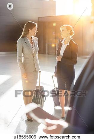 Stock Photograph - Businesswomen discussing plans while walking with their suitcase in airport. Fotosearch