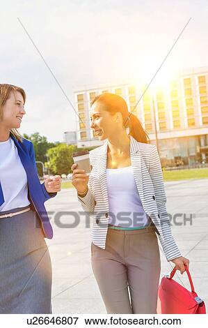 Stock Photo - Businesswomen holding a cup of coffee while talking on the road. Fotosearch