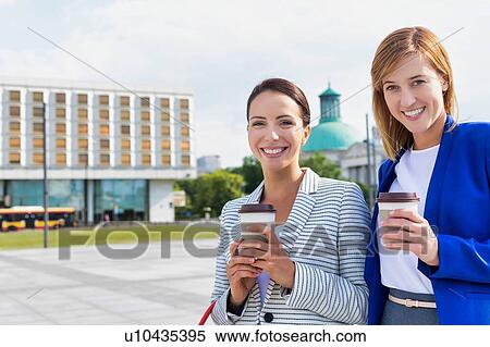 Stock Photography - Businesswomen holding a cup of coffee while talking on the road. Fotosearch