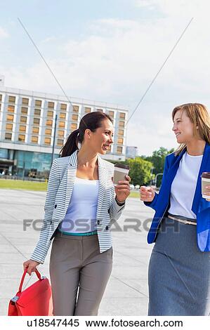 Stock Photography - Businesswomen holding a cup of coffee while talking on the road. Fotosearch