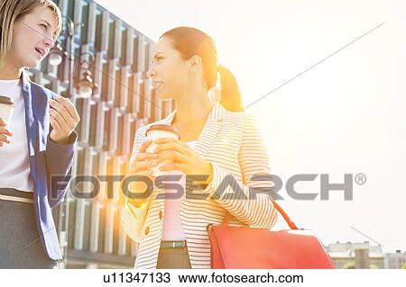 Businesswomen walking while talking outside office building View Large Photo Image Stock Image - Businesswomen walking while talking outside office building. Fotosearch