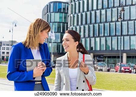 Businesswomen walking while talking outside office building View Large Photo Image Stock Image - Businesswomen walking while talking outside office building. Fotosearch