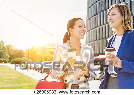 Stock Image - Businesswomen walking while talking outside office building. Fotosearch