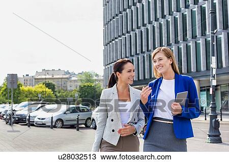 Stock Image - Businesswomen walking while talking outside office building. Fotosearch
