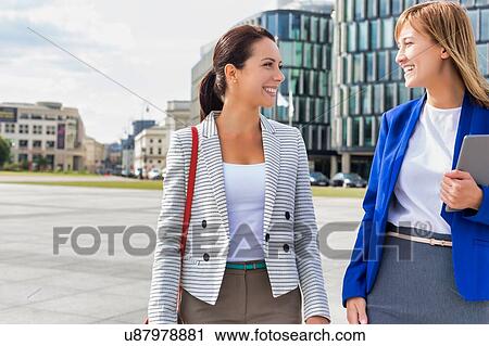 Stock Image - Businesswomen walking while talking outside office building. Fotosearch