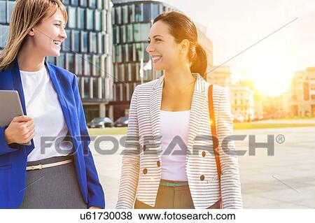 Stock Photo - Businesswomen walking while talking outside office building. Fotosearch