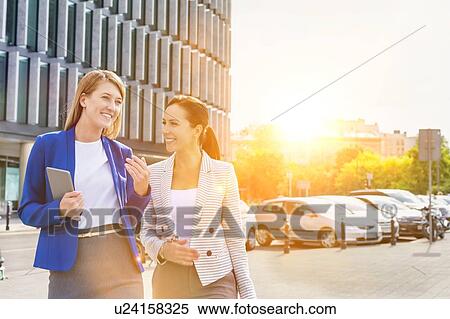 Stock Photography - Businesswomen walking while talking outside office building. Fotosearch