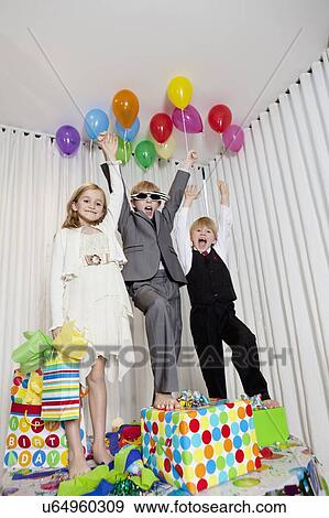 Cheerful brothers and sister with arms raised standing on table View Large Photo Image Stock Photo - Cheerful brothers and sister with arms raised standing on table. Fotosearch