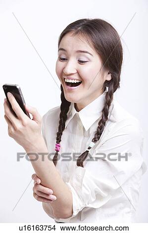 Picture - Cheerful young woman reading text message on her cell phone against white background. Fotosearch