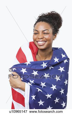 Stock Photo - Cheerful young woman wrapped in American flag over white background. Fotosearch