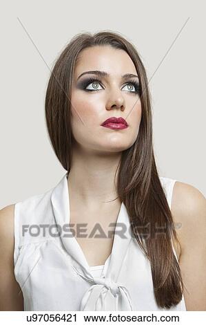 Stock Image - Close-up of a beautiful young woman looking up over gray background. Fotosearch