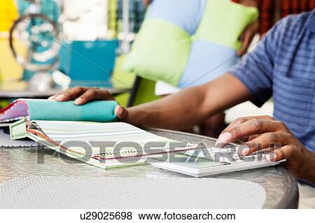 Stock Photo - Close up of designer looking at samples of cloth and calculating price. Fotosearch