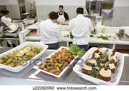 Stock Image - Close-up of foodstuff in serving dishes with chefs working in kitchen. Fotosearch