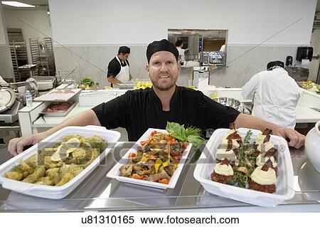 Stock Photography - Close-up of foodstuff in serving dishes with chefs in kitchen. Fotosearch