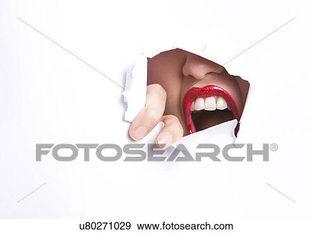 Stock Photo - Close-up of furious young woman with red lips trying to break free from paper wall. Fotosearch