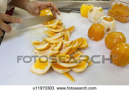 Stock Image - Close-up of hands slicing oranges with knife. Fotosearch