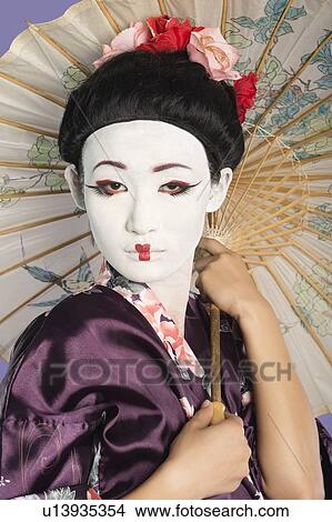 Close-up of Japanese woman with painted face holding parasol against purple background View Large Photo Image Picture - Close-up of Japanese woman with painted face holding parasol against purple background. Fotosearch