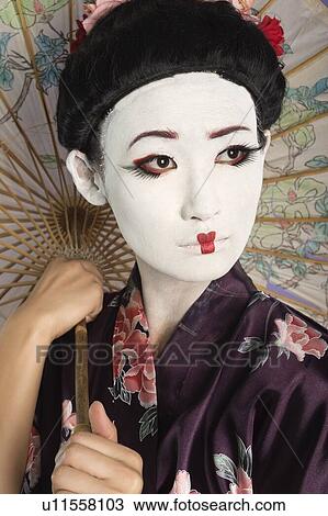 Stock Image - Close-up of Japanese woman with painted face holding parasol. Fotosearch