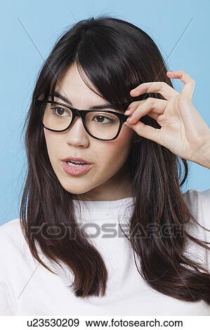 Stock Photo - Close-up of mixed race young woman wearing eyeglasses over blue background. Fotosearch