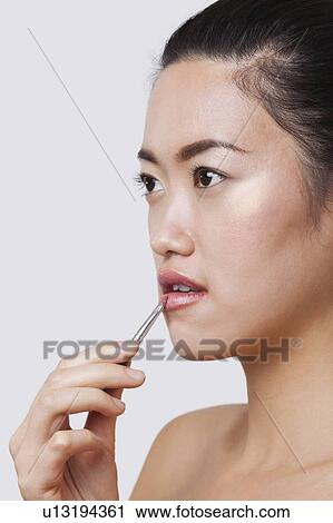 Close-up of young woman applying lip gloss with brush over white background View Large Photo Image Stock Image - Close-up of young woman applying lip gloss with brush over white background. Fotosearch