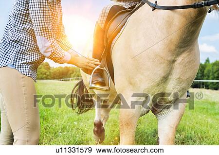 Close up photo of mature woman putting young woman feet on stirrup iron View Large Photo Image Stock Photo - Close up photo of mature woman putting young woman feet on stirrup iron . Fotosearch