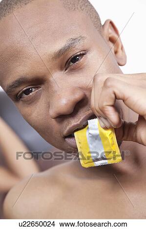 Close-up portrait of young man practicing safe sex by using condom View Large Photo Image Picture - Close-up portrait of young man practicing safe sex by using condom. Fotosearch